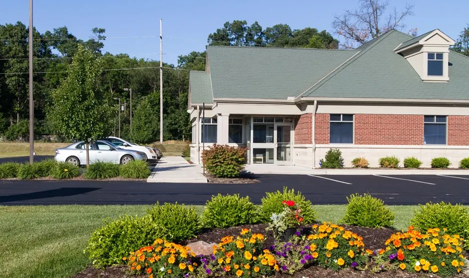 The front of Sylvania Smile Design: brick, a green metal roof and a flower bed by the lawn.
